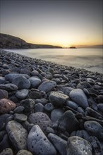 View of the sunrise over the Atlantic. View over a stone beach on a volcanic island. Cold lava