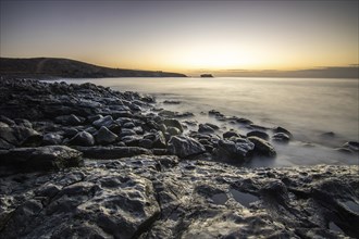 View of the sunrise over the Atlantic. View over a stone beach on a volcanic island. Cold lava