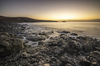 View of the sunrise over the Atlantic. View over a stone beach on a volcanic island. Cold lava