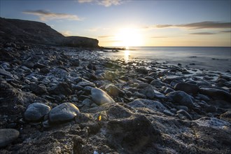 View of the sunrise over the Atlantic. View over a stone beach on a volcanic island. Cold lava