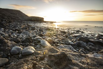 View of the sunrise over the Atlantic. View over a stone beach on a volcanic island. Cold lava