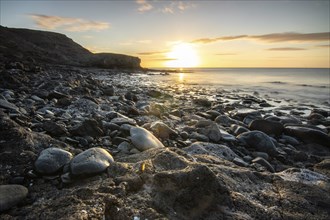 View of the sunrise over the Atlantic. View over a stone beach on a volcanic island. Cold lava