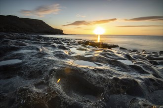 View of the sunrise over the Atlantic. View over a stone beach on a volcanic island. Cold lava