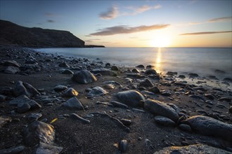 View of the sunrise over the Atlantic. View over a stone beach on a volcanic island. Cold lava