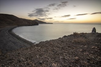 View of the sunrise over the Atlantic. A coastline and a bay with a rocky beach on a volcanic