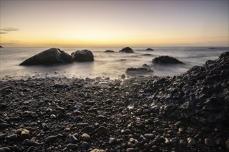 View of the sunrise over the Atlantic. View over a stone beach on a volcanic island. Cold lava