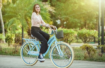 Portrait of beautiful smiling young woman riding a bicycle at sunset, looking at camera