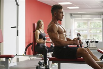 Shirtless guy trains on simulator and girl looks at him