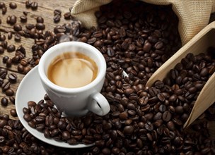 Coffee cup with burlap sack of roasted beans on rustic table, hot coffee