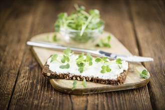 An old wooden table with healthy food (slice of bread, cream cheese and fresh cutted cress),