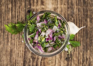 Old wooden table with fresh Chimichurri (close-up shot, selective focus)