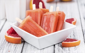Some homemade Grapefruit Popsicles (with some fresh fruits) as close-up shot (selective focus)