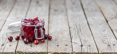 Old wooden table with fresh Preserved Cranberries (close-up shot, selective focus)