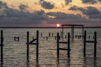 Sunset behind remains of damaged wooden pier pilings on Perdido Bay in Perdido Key, Florida