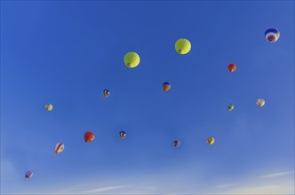 Colorful hot air balloons floating in a clear blue sky with a few clouds, creating a vibrant and