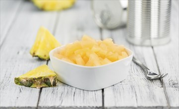 Chopped Pineapple (preserved) as high detailed close-up shot on a vintage wooden table, selective