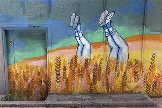 Legs of young people sticking out of a cornfield, mural at a Likada organic food shop, Exarchia