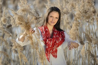 Brunette woman with a red scarf smiling in a field of tall dry grass, Bavaria