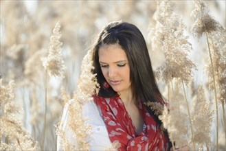 Brunette woman with a red scarf looking down surrounded by tall dry grass, Bavaria