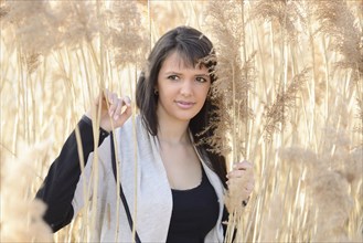 Brunette woman standing in tall dry grass, looking at the camera outdoors, Bavaria