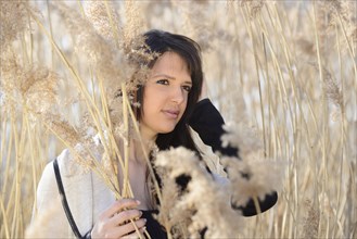 A woman with dark hair stands pensively among reeds, with soft light illuminating her face, Bavaria