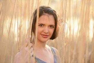 A young woman with brown hair smiling in a field of reeds with sunlight streaming through, Bavaria