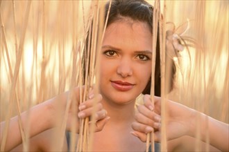 A young woman with brown hair stands amidst reeds, with sunlight filtering through them, Bavaria