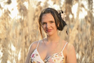 A woman in a floral dress smiling among tall reeds during golden hour, Bavaria