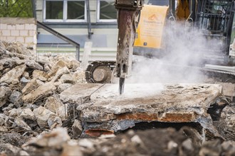 Demolition work on a building with an excavator breaking up concrete. Dust and debris are scattered