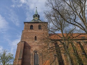 Impressive Gothic-style brick church tower surrounded by trees under a partly cloudy sky, lüneburg,