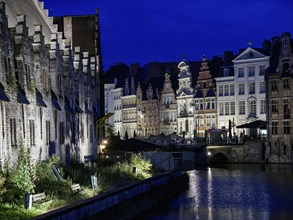 Historic buildings on the riverbank at night, illuminated and reflecting in the water, Ghent,