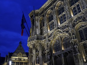 Monumental historic building with detailed facades and flags against a dramatic evening sky, Ghent,