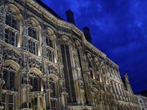 Complex gothic façade details of an illuminated building at night, dramatic sky, Ghent, Belgium,