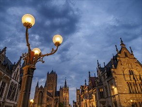 Illuminated street lamp in front of historic buildings at dusk under a cloudy sky, Ghent, Belgium,