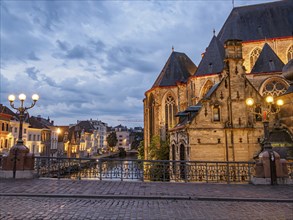 Gothic church by a river at dusk with illuminated bridge and streetlights, Ghent, Belgium, Europe
