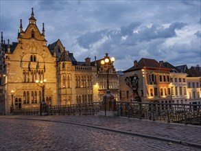 Historic buildings and cobblestone street with glowing lanterns at dusk, Ghent, Belgium, Europe