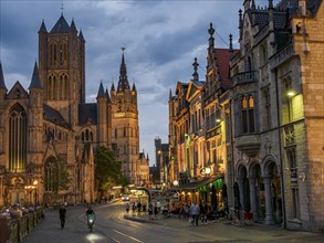 Evening street scene with church and historic buildings, illuminated and lively, Ghent, Belgium,