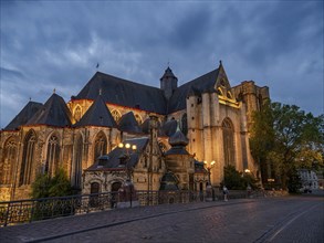 Large illuminated church at dusk, with a street in the foreground and cloudy sky, Ghent, Belgium,