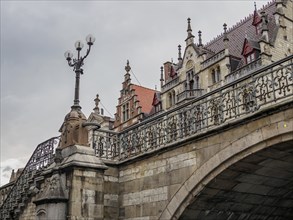 Stone bridge with ornate lanterns and historic buildings in the background under a cloudy sky,