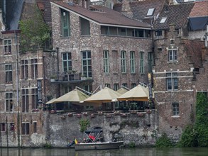 Old brick buildings with terraces and boats along a riverbank in the city, Ghent, Belgium, Europe