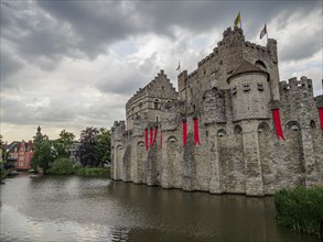 Medieval castle with stone walls and red flags on a moat under a cloudy sky, Ghent, Belgium, Europe