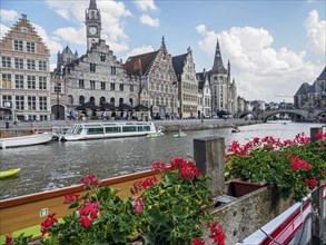A river with boats and blooming flowers in the foreground, flanked by historic buildings and