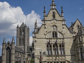 An impressive historic building and a Gothic church with towers against a blue sky, Ghent, Belgium,