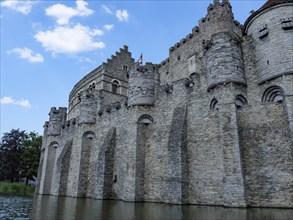 Medieval castle with fortification towers by a river under a blue sky, Ghent, Belgium, Europe