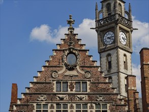 A striking clock tower and the gable of a brick house stand out against a blue sky, Ghent, Belgium,