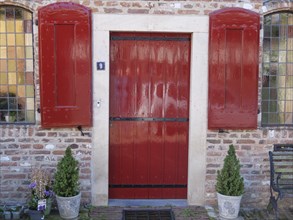 A red door with matching shutters and two potted plants in front of it, Doesburg, Netherlands