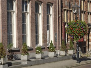 Facade of a brick building with large windows and plants in pots and a hanging flower basket,
