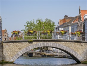 Stone bridge over a canal, decorated with flowers, surrounded by historic buildings, Bruges,