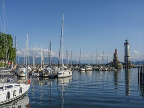 Boats in the harbour with a lighthouse and a lion statue in the background under a blue sky,