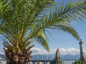 Palm tree in front of a lion statue and a lighthouse, calm water and boats in the background,